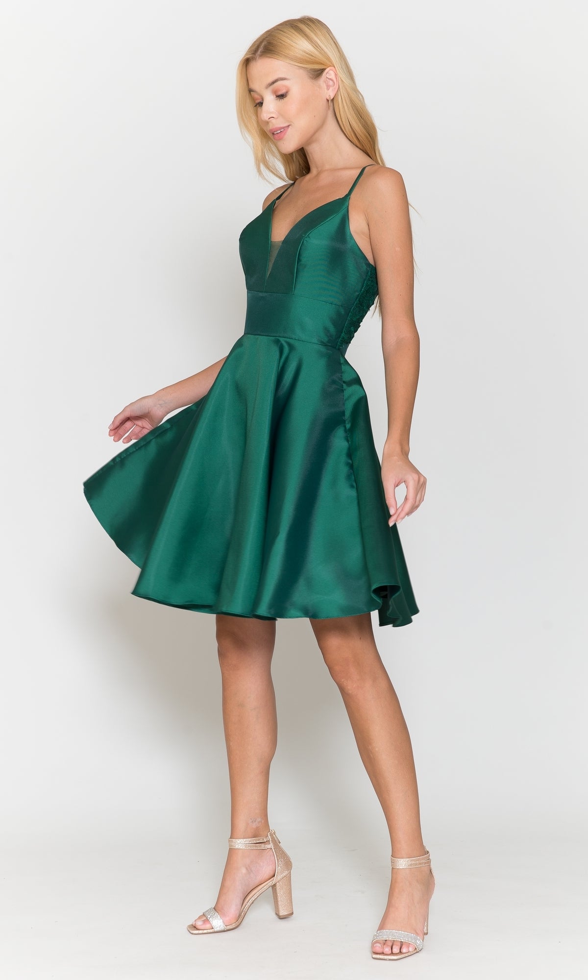 A woman in the Lace-Back Short A-Line Homecoming Dress 8698—sleeveless, deep green with a V-neck and knee-length hem—stands against a plain white background, paired with strappy heels.